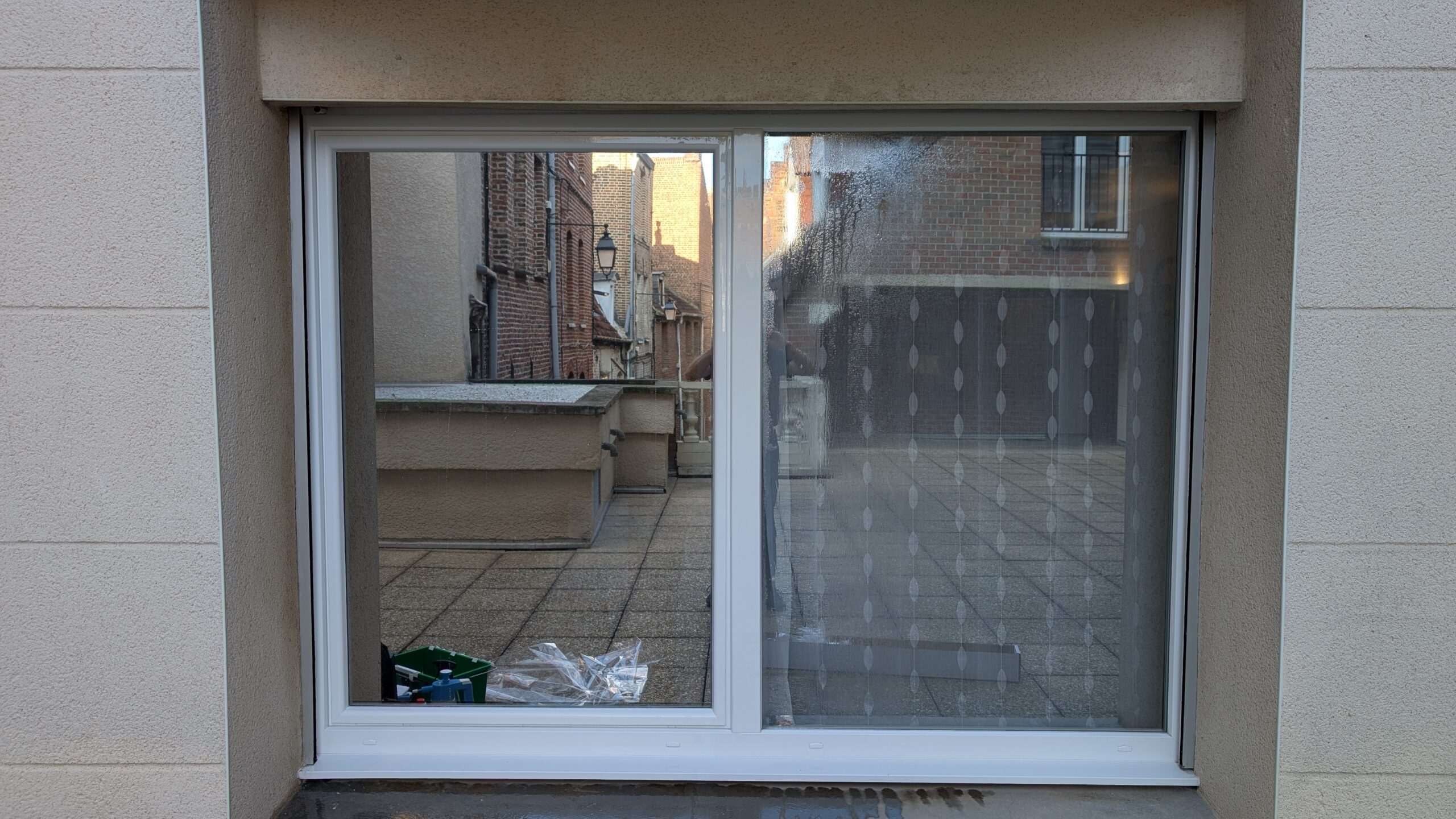 Comparatif sur une baie vitrée avec un film solaire anti-regard à gauche et un vitrage classique sans film à droite laissant voir le rideau à l'intérieur.