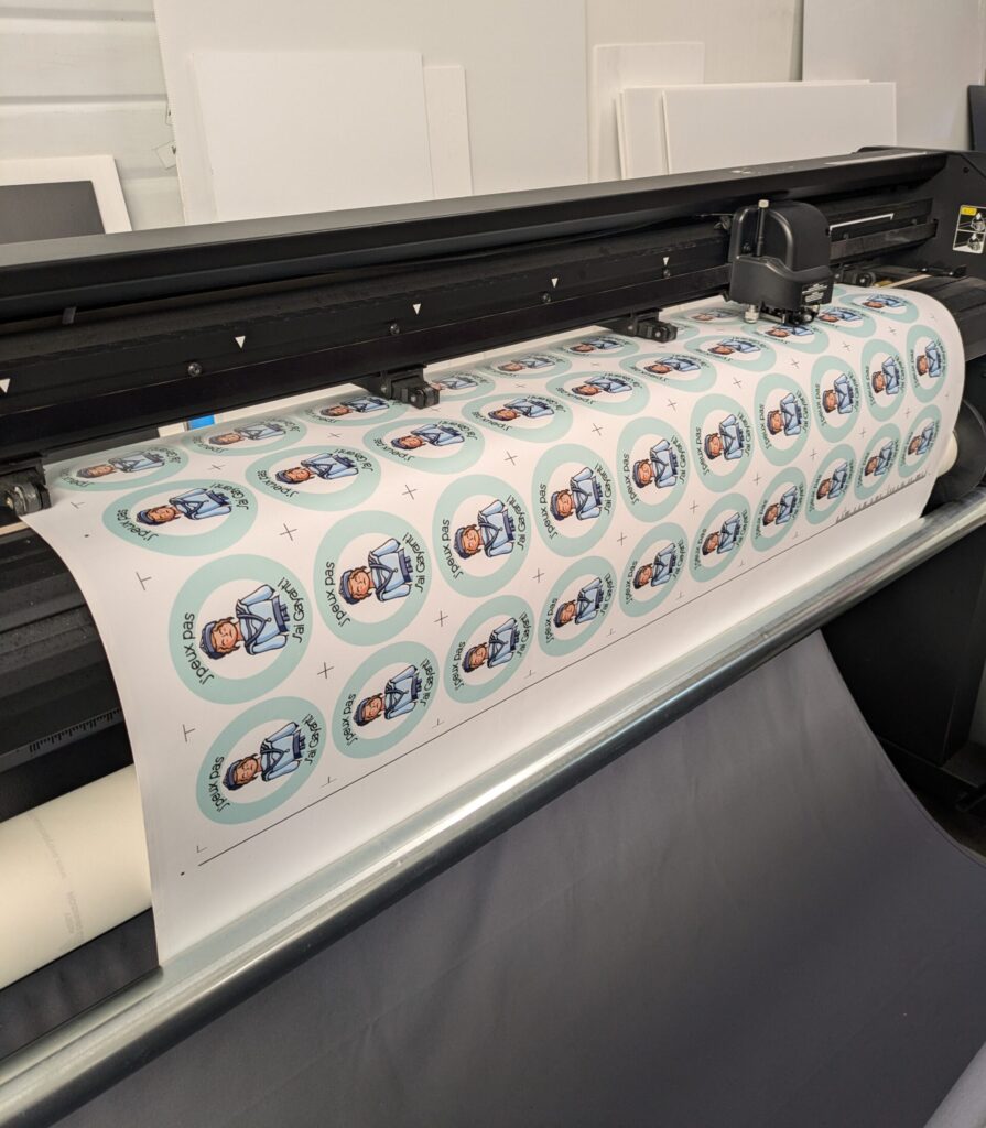 Machine d'impression en train de découper une planche de stickers personnalisés "J'peux pas j'ai Gayant" pour l'Office de Tourisme de Douai par DM Création.